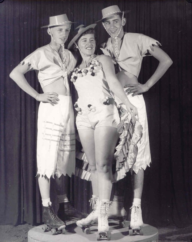 Three performers in white outfits and hats pose together on roller skates in front of a dark curtain.